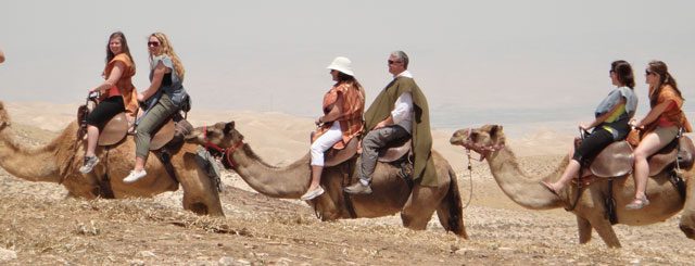 The group enjoys a camel ride through the desert hills