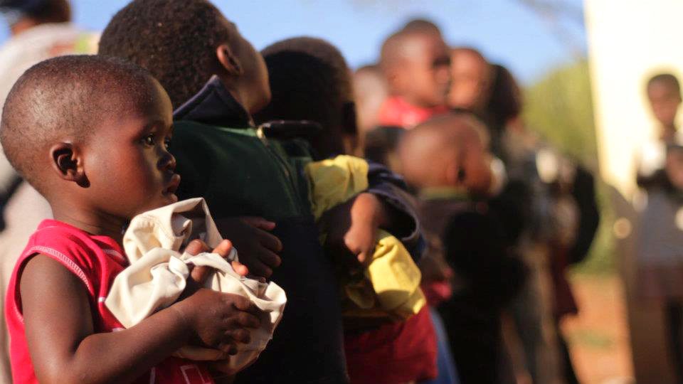 Young children standing in line outside holding clothes