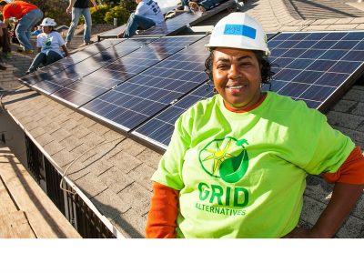 Woman in green shirt and hardhat next to solar panel