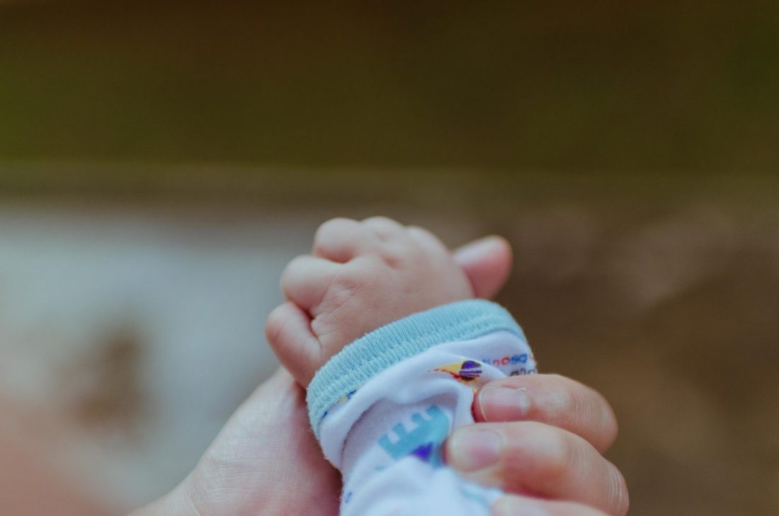 adult holding newborn baby hand