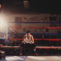 young boxer sitting on ropes inside ring