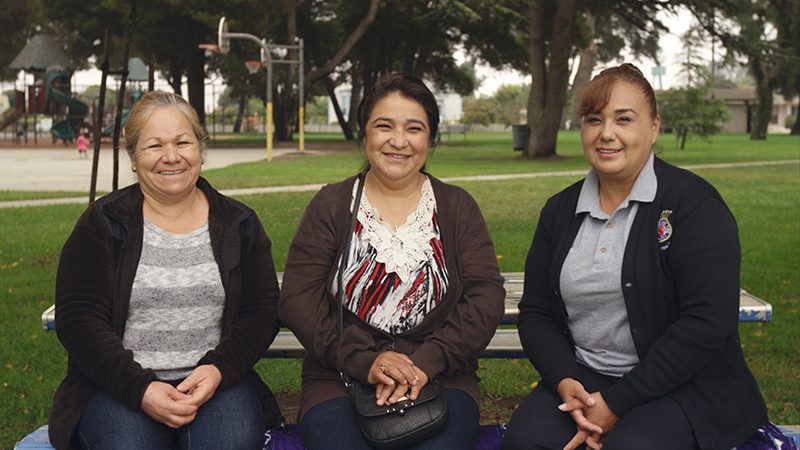 Three women sitting on bench outside smiling