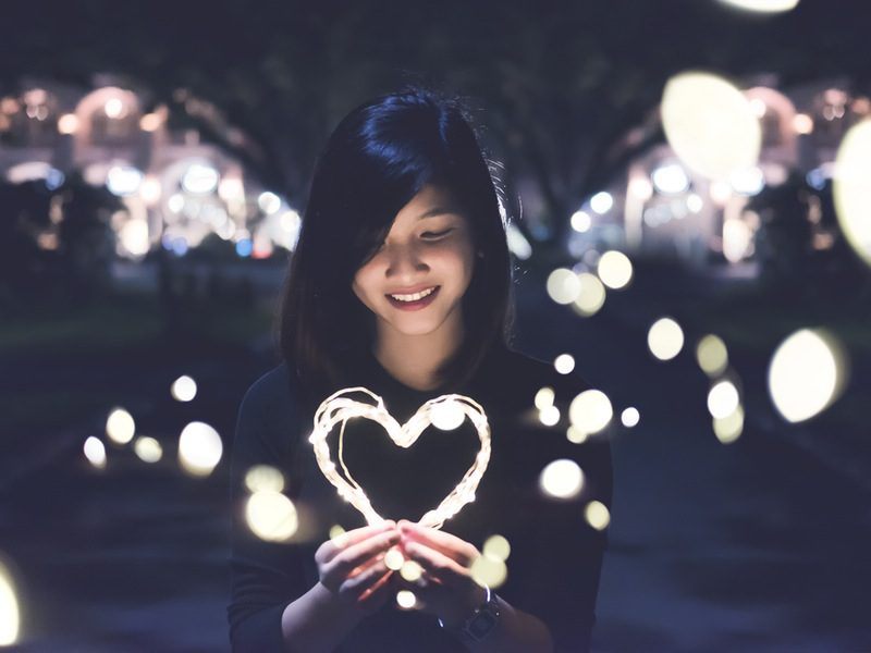 Girl smiling while holding illuminated heart