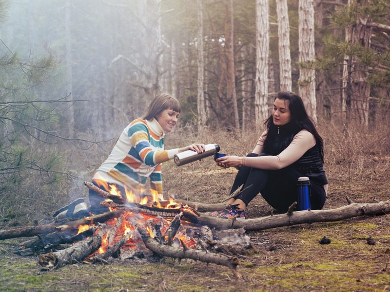 one person pouring drink for friend while camping