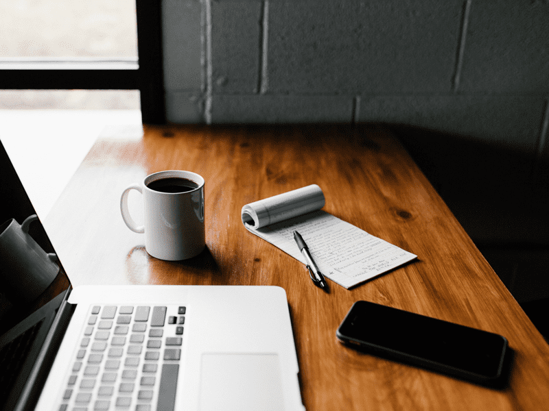 Laptop, phone, coffee, and notebook on table