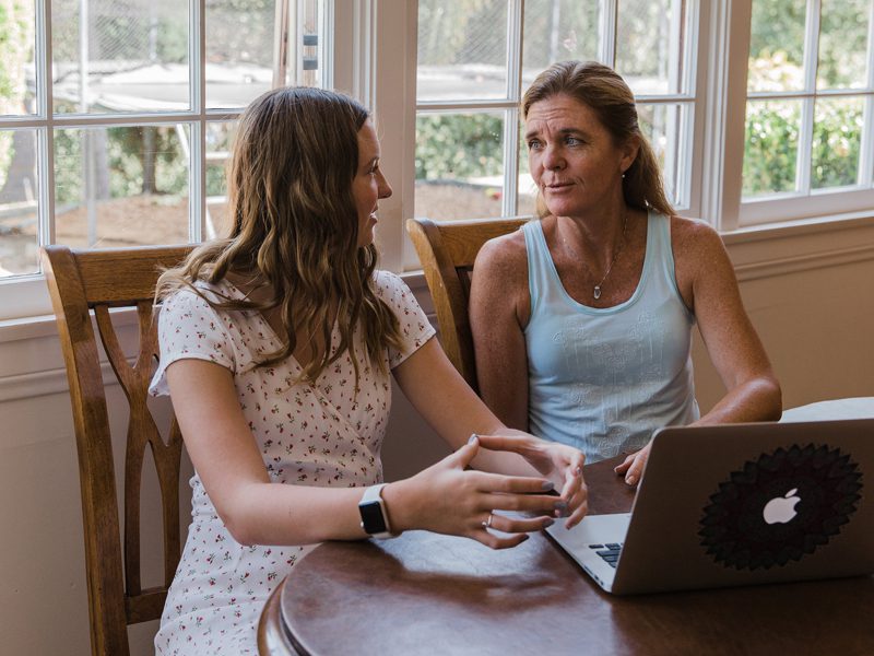 Mother and daughter sitting at table and talking in front of computer