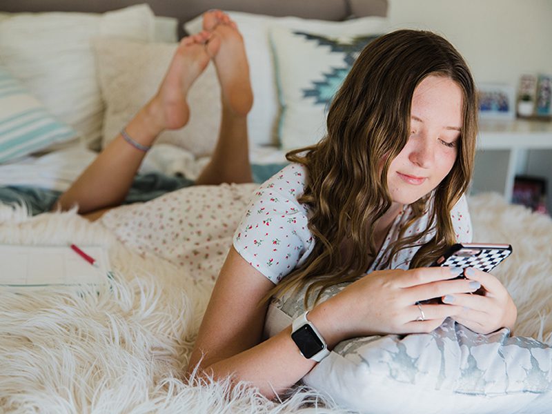 Girl laying in bed and smiling at cell phone