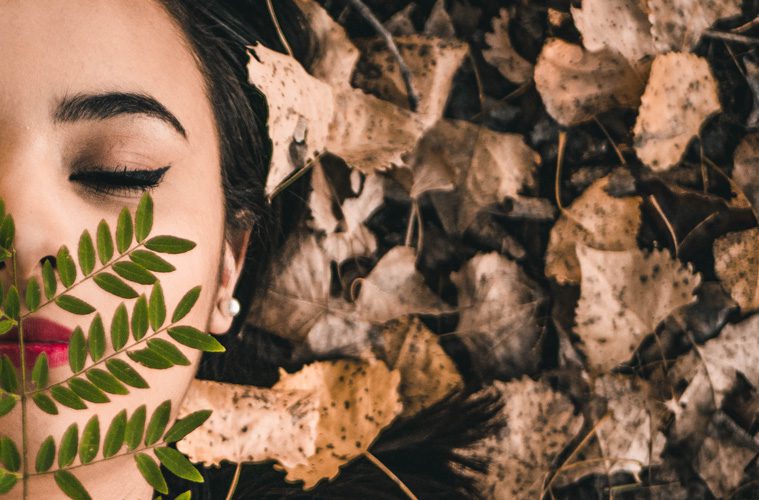 woman laying with eyes closed next to leaves