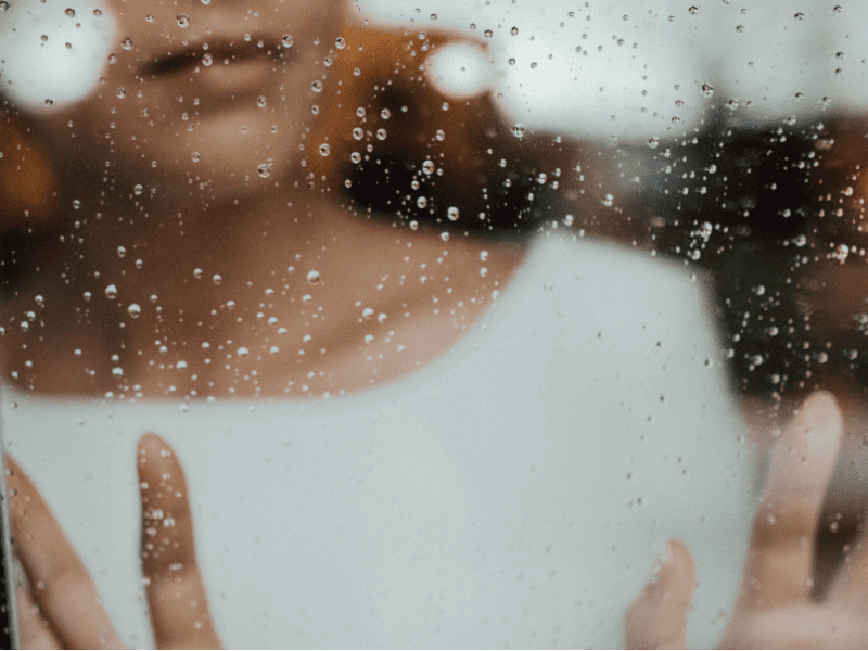 woman looking through window with water on it