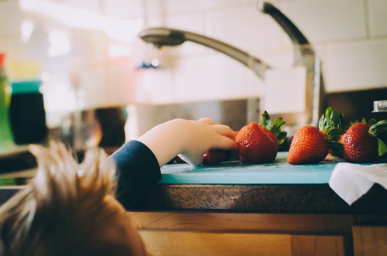 child reaching for strawberries by sink
