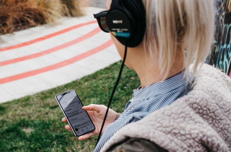 woman outside looking at phone with headphones on