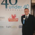 Man in suit standing in front of 40 under 40 poster