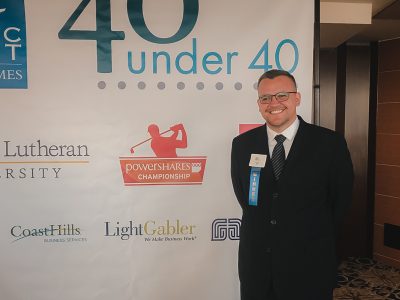 Man in suit standing in front of 40 under 40 poster