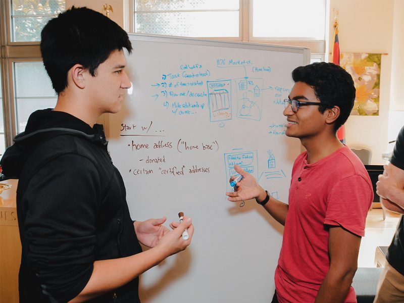 Two youth write discussing next to whiteboard