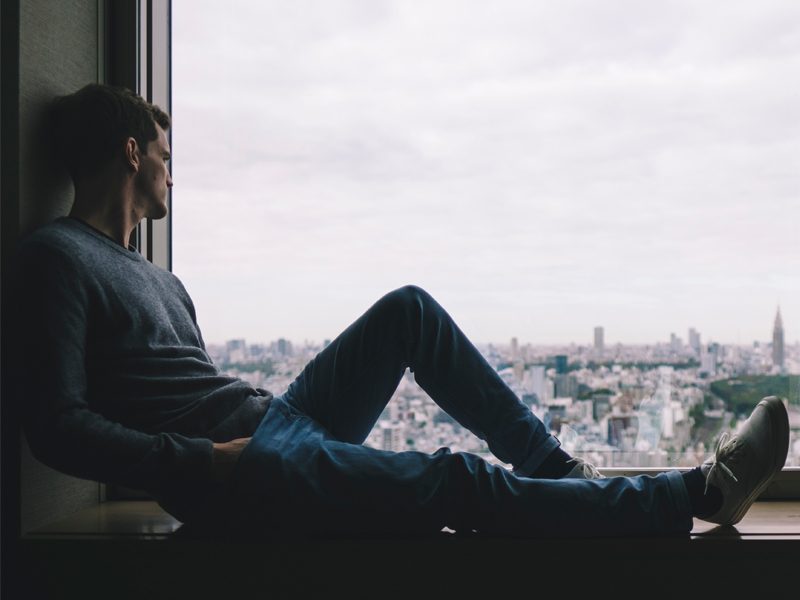 man sitting on ledge looking out at city