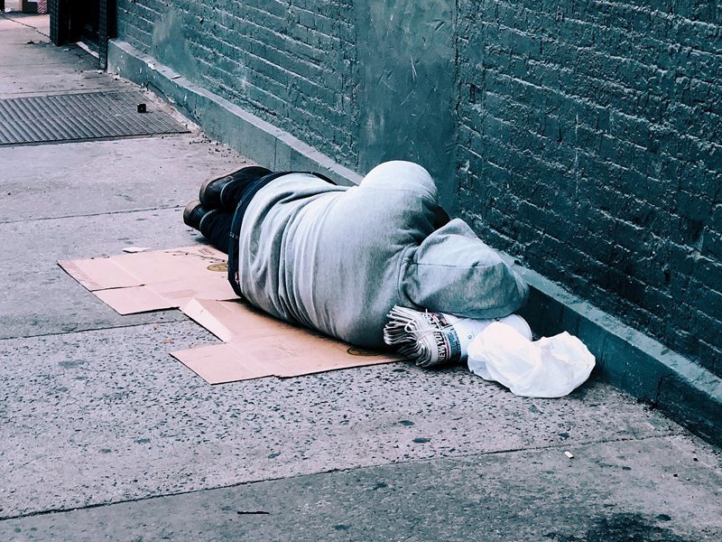 Man in sweatshirt sleeping on cardboard on the street
