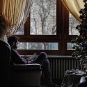 man sitting by window next to Christmas tree