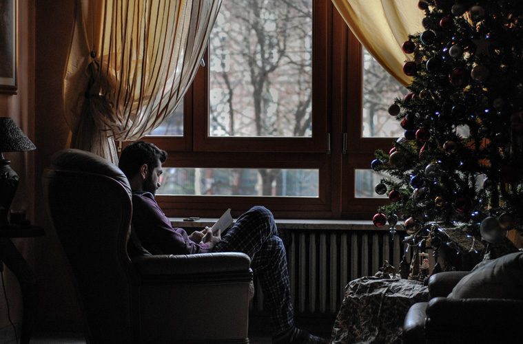 man sitting by window next to Christmas tree
