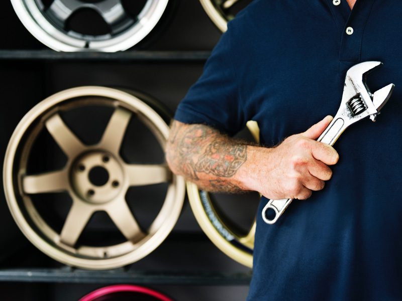 Mechanic with tattoo holding wrench in front of wheels