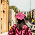 Female Graduate in Red Cap and Gown Walking Down Street