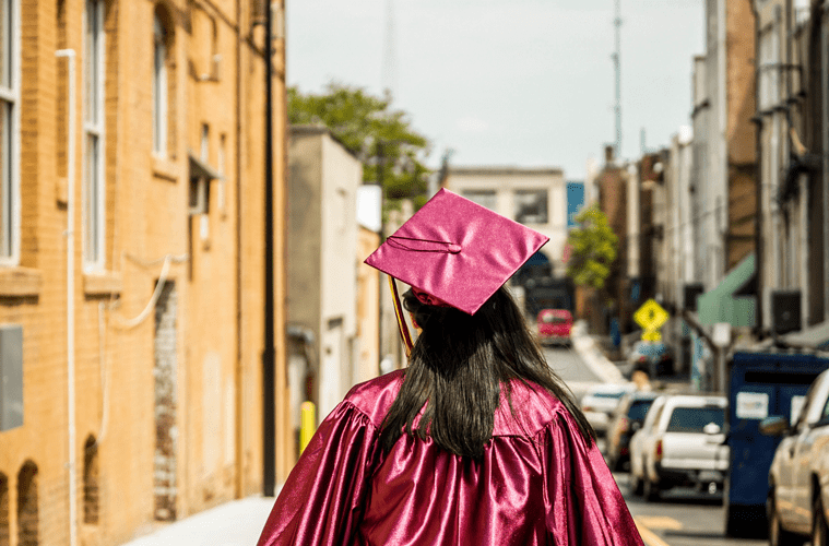 Female Graduate in Red Cap and Gown Walking Down Street