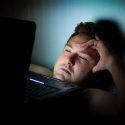 Man Looking Distressed with Laptop on Chest