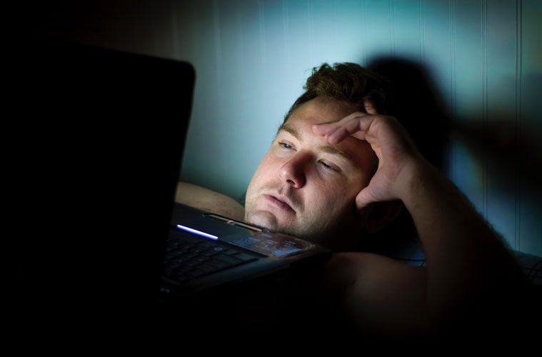 Man Looking Distressed with Laptop on Chest