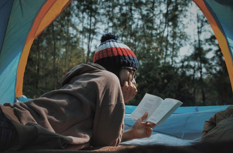 Person Reading Book in Open Tent with Trees in Background