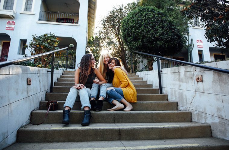 Three female friends laughing together while sitting on stairs