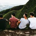Four Male Friends Sitting on Mountain Ledge Laughing