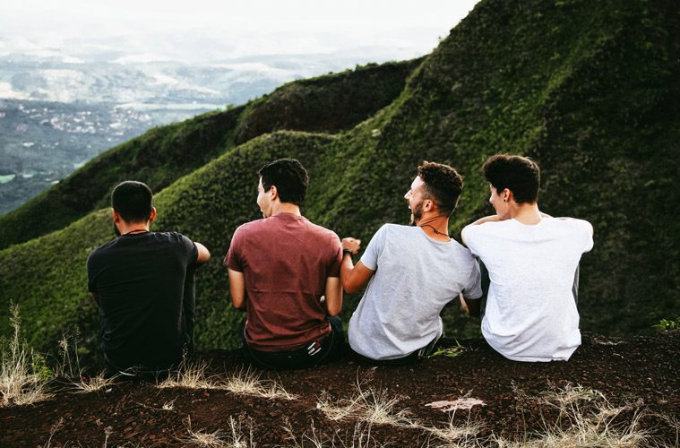 Four Male Friends Sitting on Mountain Ledge Laughing