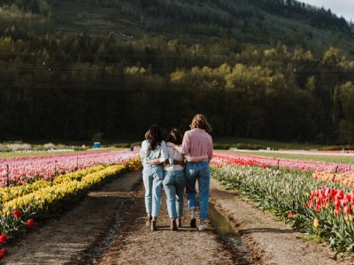 Female Friends with Arms Around Each Other Walking Through Flower Field