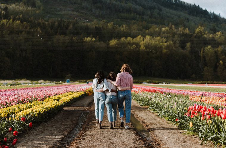 Female Friends with Arms Around Each Other Walking Through Flower Field