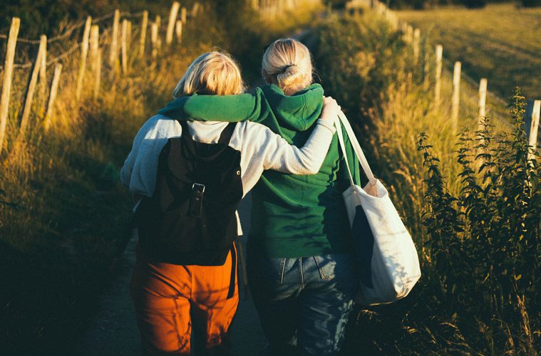 female friends walking with arm around shoulders