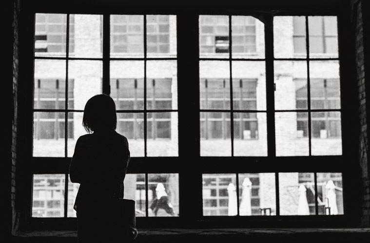 black and white photo of woman looking outside window