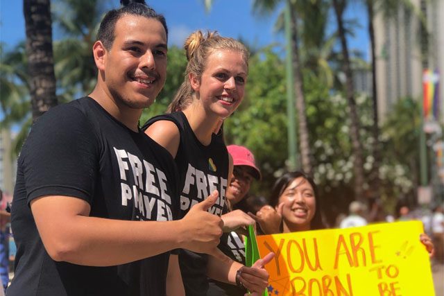 Revolution Hawaii Members at Parade with Sign in Background 