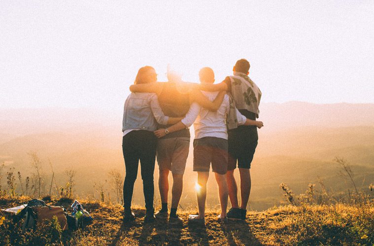 four people with arms around each other outside