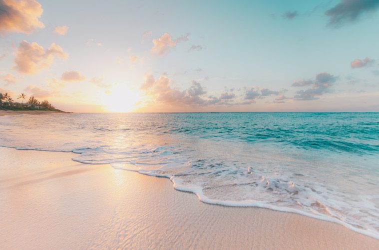 water on sandy shore with sun behind