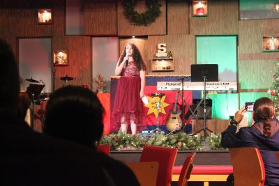 Young girl sings a song on stage at a Christmas event.
