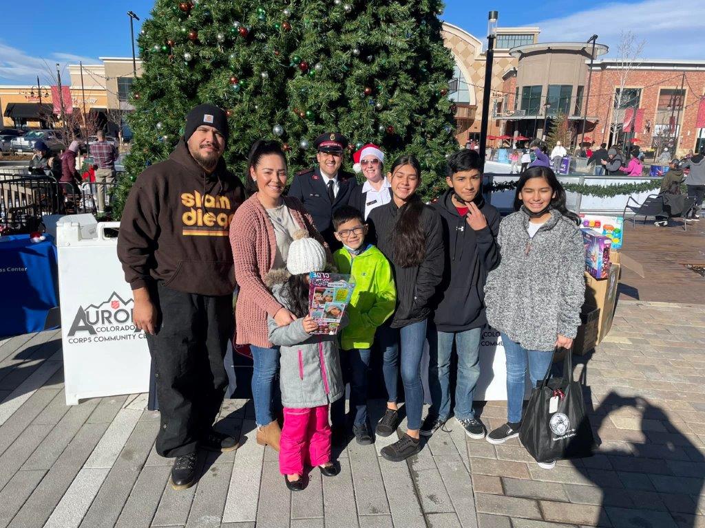 People smile and stand in front of a Christmas tree outside