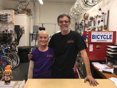 man and woman stand behind the counter of a bike shop smiling
