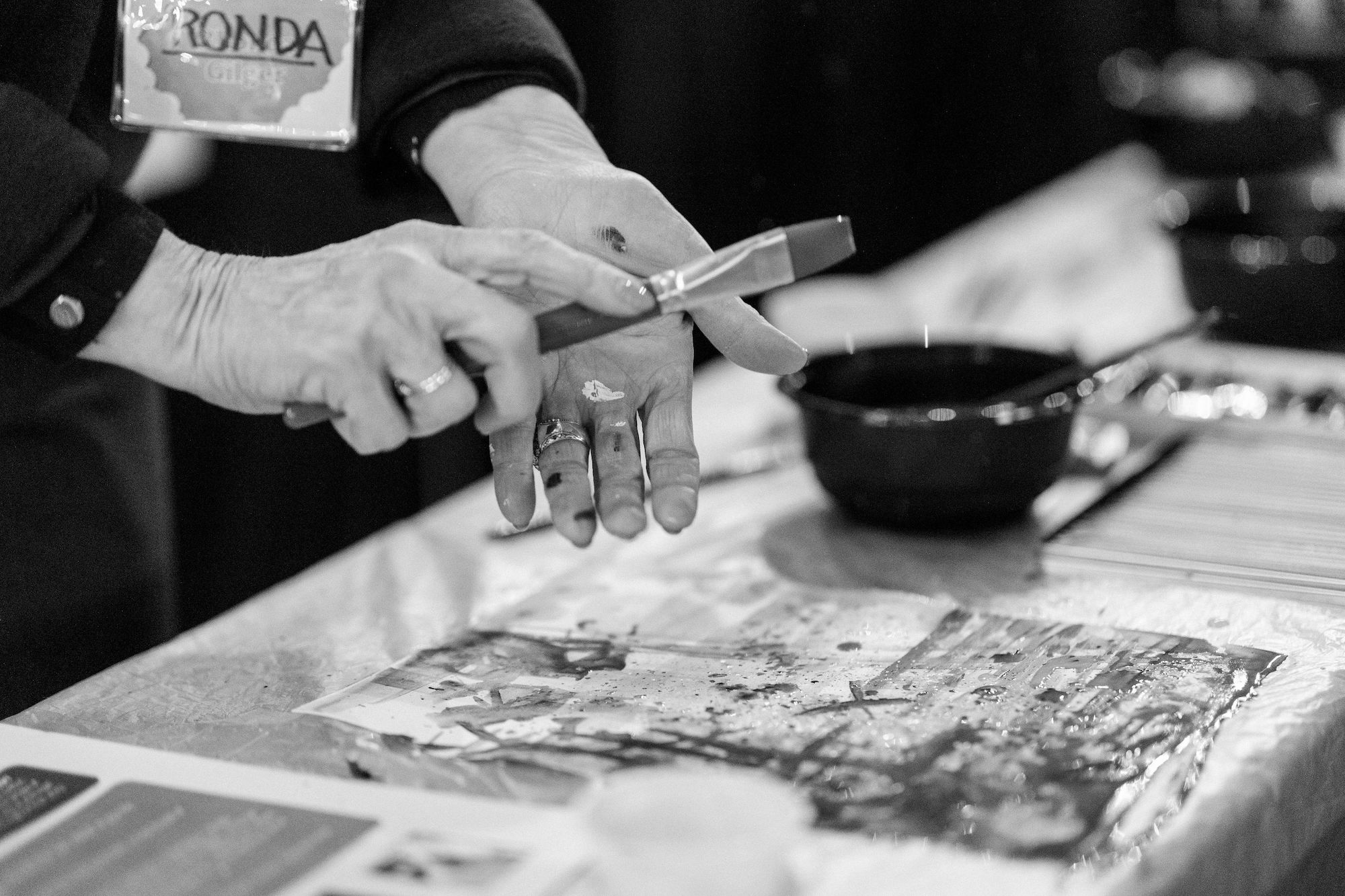 close up black and white photo of woman's hands using a paint brush to paint on canvas