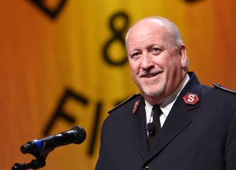 male salvation army officer speaks into a microphone on stage