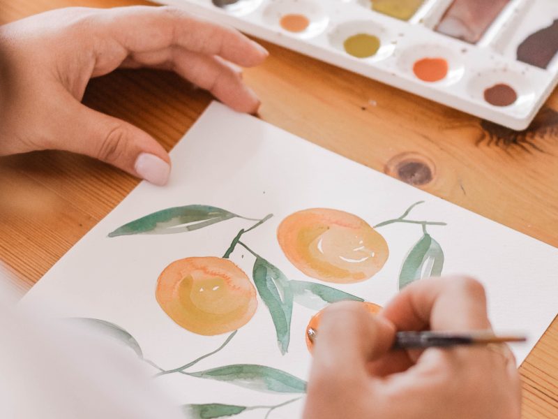 close up on artist using a paintbrush to paint oranges on paper