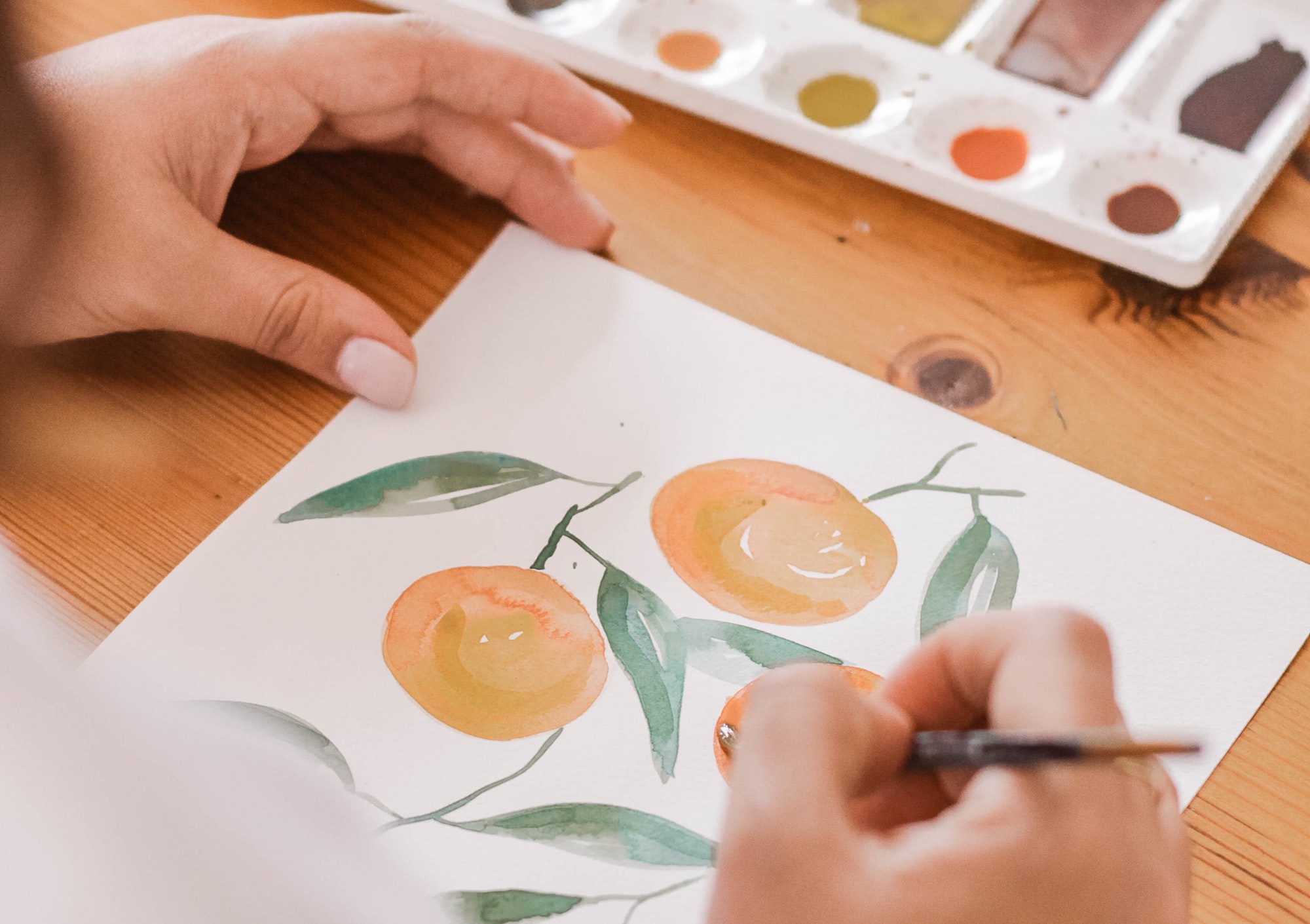 close up on artist using a paintbrush to paint oranges on paper